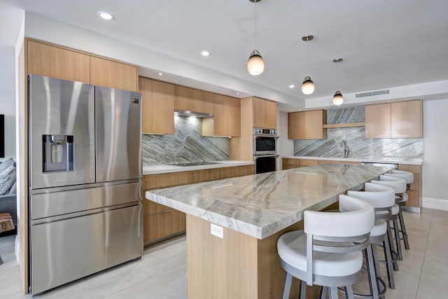 kitchen featuring light stone countertops, a center island, decorative light fixtures, stainless steel appliances, and backsplash