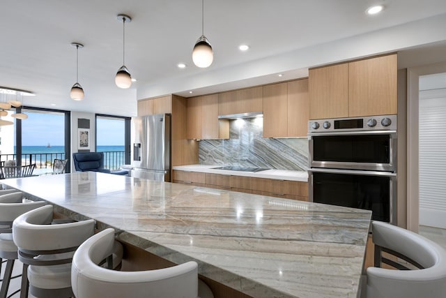 kitchen featuring light stone countertops, pendant lighting, appliances with stainless steel finishes, tasteful backsplash, and a water view