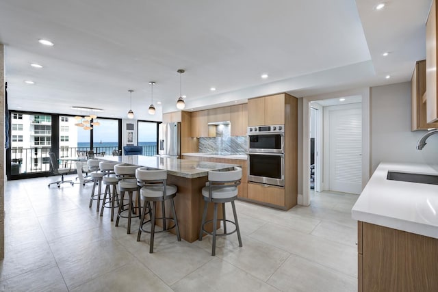 kitchen with hanging light fixtures, sink, light stone counters, a wall of windows, and stainless steel appliances