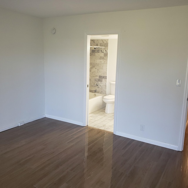 unfurnished bedroom with ensuite bathroom and dark wood-type flooring