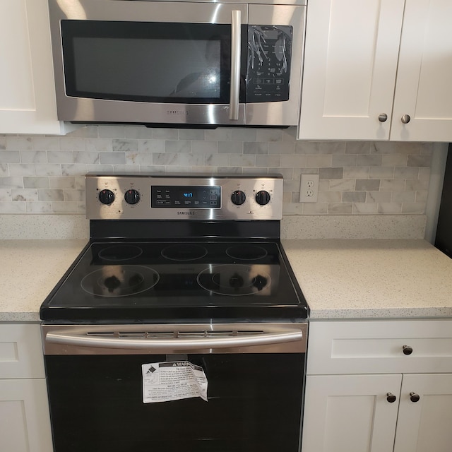 kitchen with appliances with stainless steel finishes, white cabinets, light stone counters, and tasteful backsplash