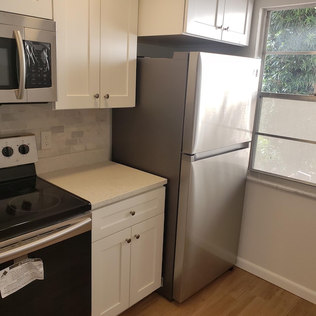 kitchen featuring light hardwood / wood-style floors, stainless steel appliances, light stone countertops, white cabinets, and backsplash