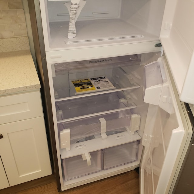 interior details with dark wood-type flooring, fridge, light stone countertops, and white cabinetry