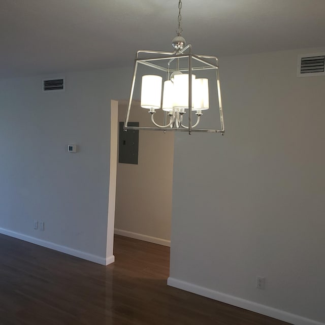 spare room featuring electric panel, dark wood-type flooring, and a chandelier