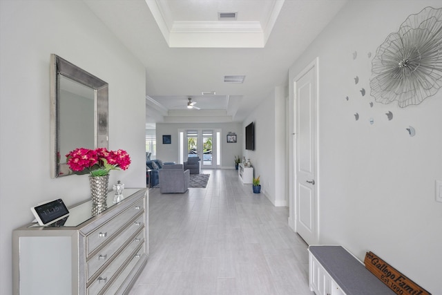 hallway with ornamental molding, light hardwood / wood-style flooring, and a tray ceiling