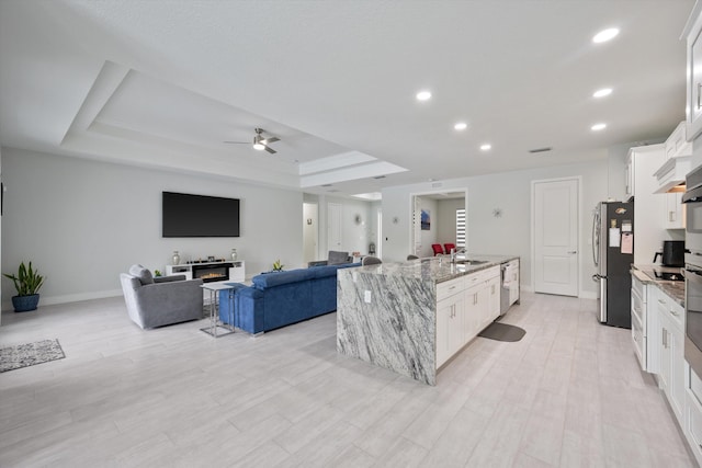 kitchen with stainless steel appliances, white cabinetry, a raised ceiling, light stone countertops, and a kitchen island with sink