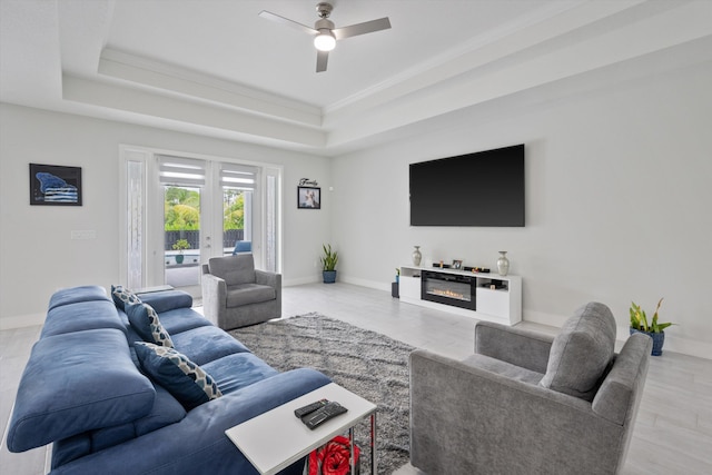 living room with a raised ceiling, light wood-type flooring, crown molding, ceiling fan, and french doors