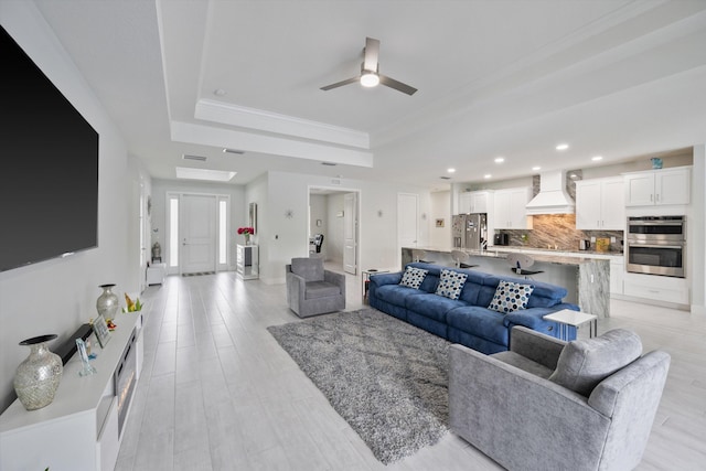 living room featuring ceiling fan, a tray ceiling, ornamental molding, and light hardwood / wood-style flooring