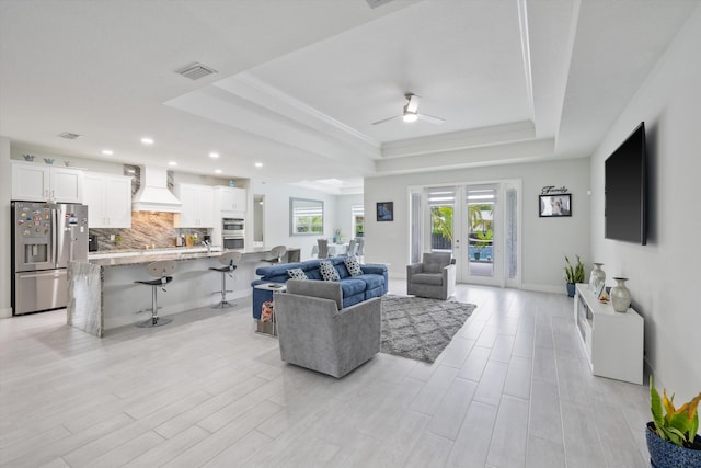 living room featuring light wood-type flooring, a raised ceiling, ceiling fan, and french doors