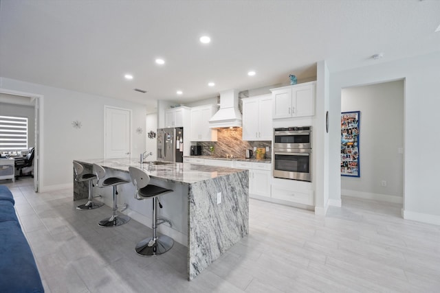 kitchen featuring stainless steel appliances, a large island, white cabinetry, a kitchen breakfast bar, and custom exhaust hood