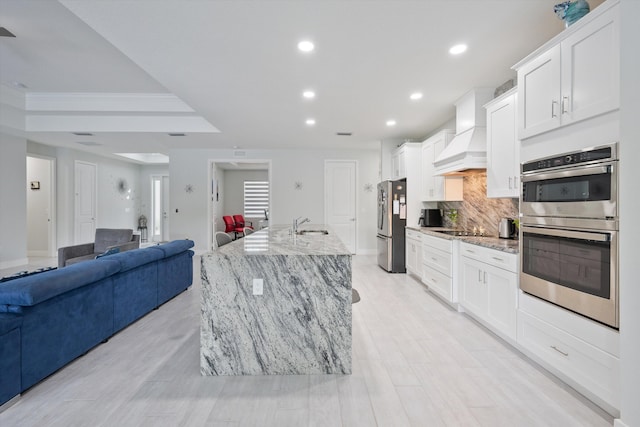 kitchen featuring stainless steel appliances, a large island, white cabinetry, light stone counters, and custom range hood