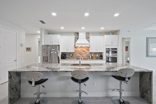 kitchen with a kitchen bar, white cabinetry, premium range hood, and appliances with stainless steel finishes