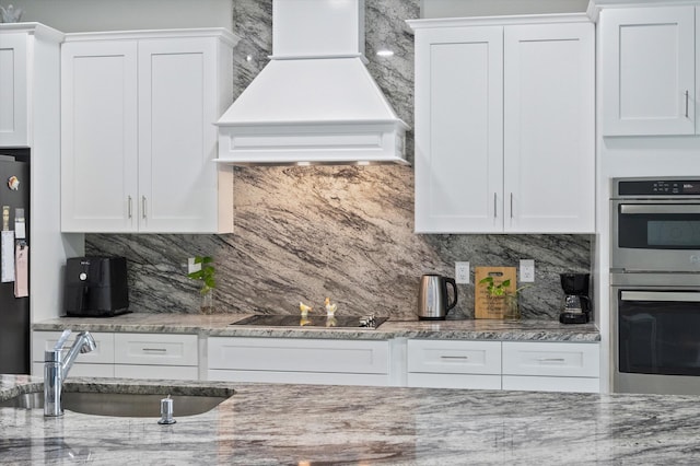 kitchen with sink, white cabinets, backsplash, premium range hood, and black appliances