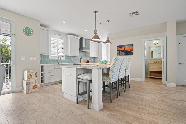 kitchen featuring white cabinetry, a breakfast bar, decorative light fixtures, a kitchen island, and wall chimney exhaust hood