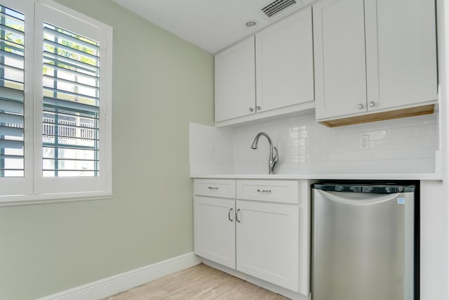 kitchen featuring white cabinets, stainless steel dishwasher, decorative backsplash, sink, and light wood-type flooring