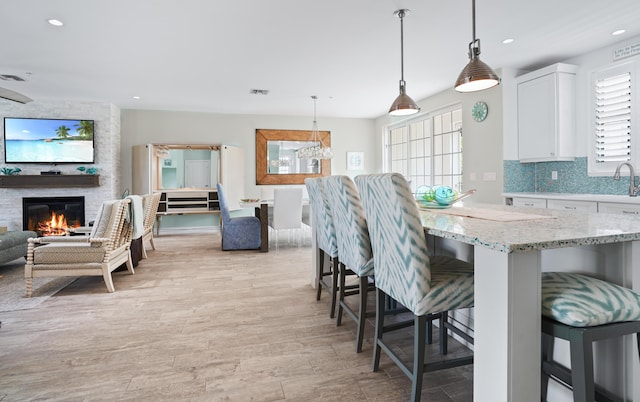 kitchen featuring a kitchen bar, light stone counters, white cabinetry, plenty of natural light, and hanging light fixtures