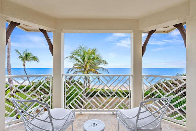 view of patio / terrace featuring a balcony, a water view, and a view of the beach