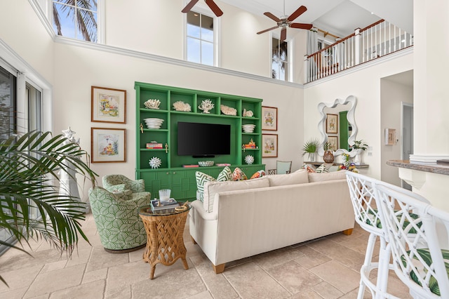 living area featuring ceiling fan, a high ceiling, and stone tile flooring