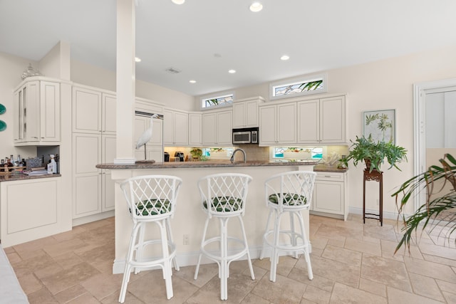 kitchen featuring stainless steel microwave, decorative backsplash, visible vents, and a kitchen breakfast bar