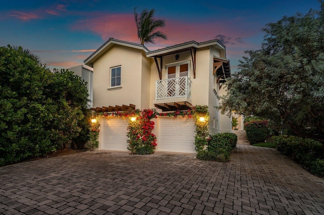 view of front of home with a balcony, an attached garage, decorative driveway, and stucco siding