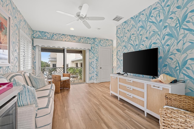 living room with wallpapered walls, visible vents, baseboards, light wood-style flooring, and ceiling fan