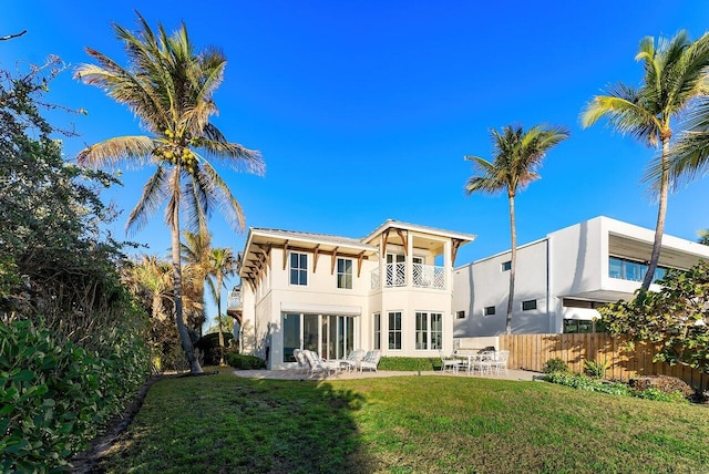 back of property with stucco siding, a lawn, a patio area, fence, and a balcony