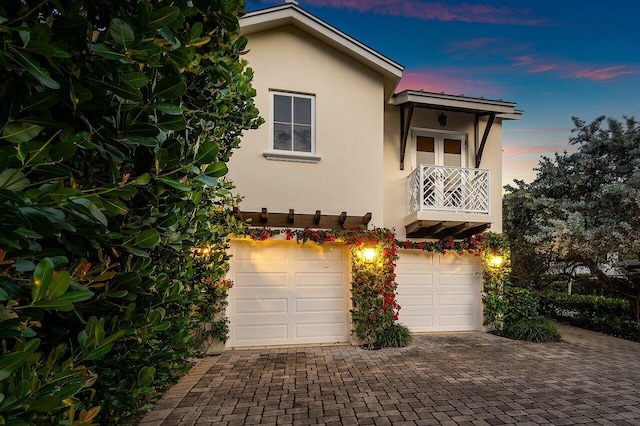 exterior space featuring a balcony, a garage, decorative driveway, and stucco siding