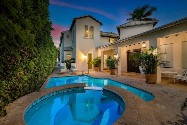 rear view of house with a pool with connected hot tub, a patio, and stucco siding