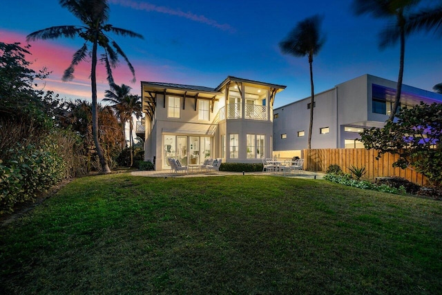 rear view of house featuring a balcony, fence, a lawn, and stucco siding