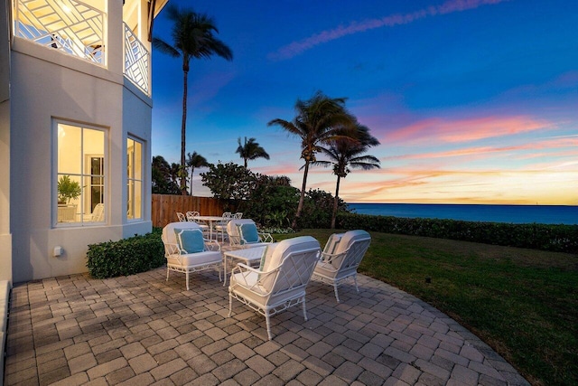 patio terrace at dusk featuring outdoor dining space, a water view, and fence