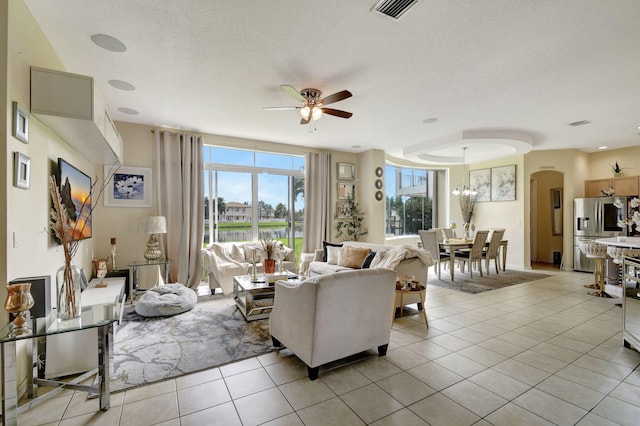 living room featuring ceiling fan with notable chandelier, light tile patterned flooring, and a textured ceiling