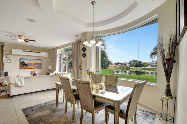 tiled dining space with a healthy amount of sunlight, a water view, ceiling fan with notable chandelier, and a tray ceiling