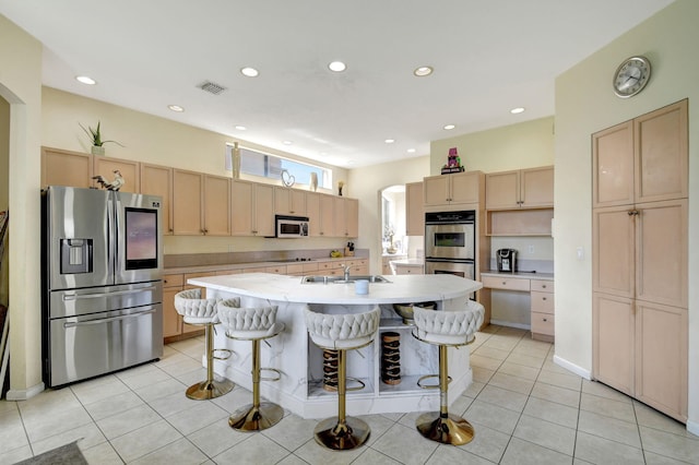 kitchen featuring stainless steel appliances, a center island with sink, a kitchen bar, and light tile patterned floors