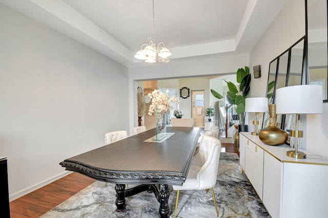 dining space with a raised ceiling, hardwood / wood-style flooring, and a notable chandelier