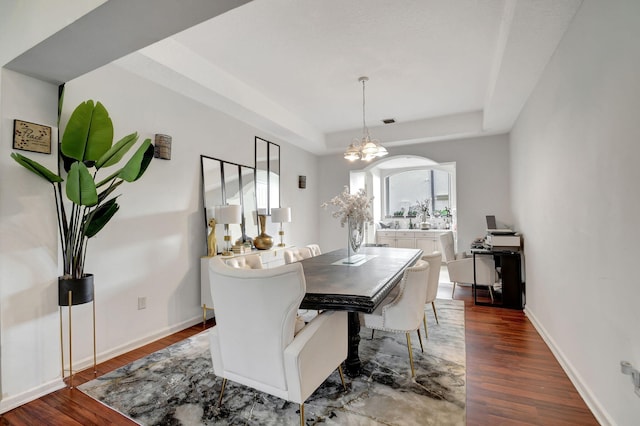 dining space featuring dark wood-type flooring, a notable chandelier, and a tray ceiling