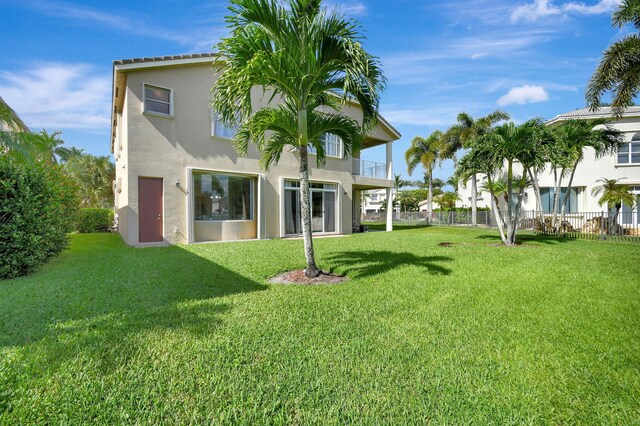 rear view of property featuring a balcony and a yard