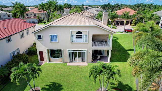 rear view of house with a balcony, a patio, and a lawn