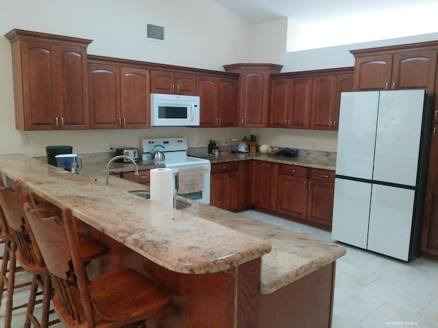 kitchen featuring white appliances, kitchen peninsula, a high ceiling, light tile patterned floors, and a kitchen breakfast bar