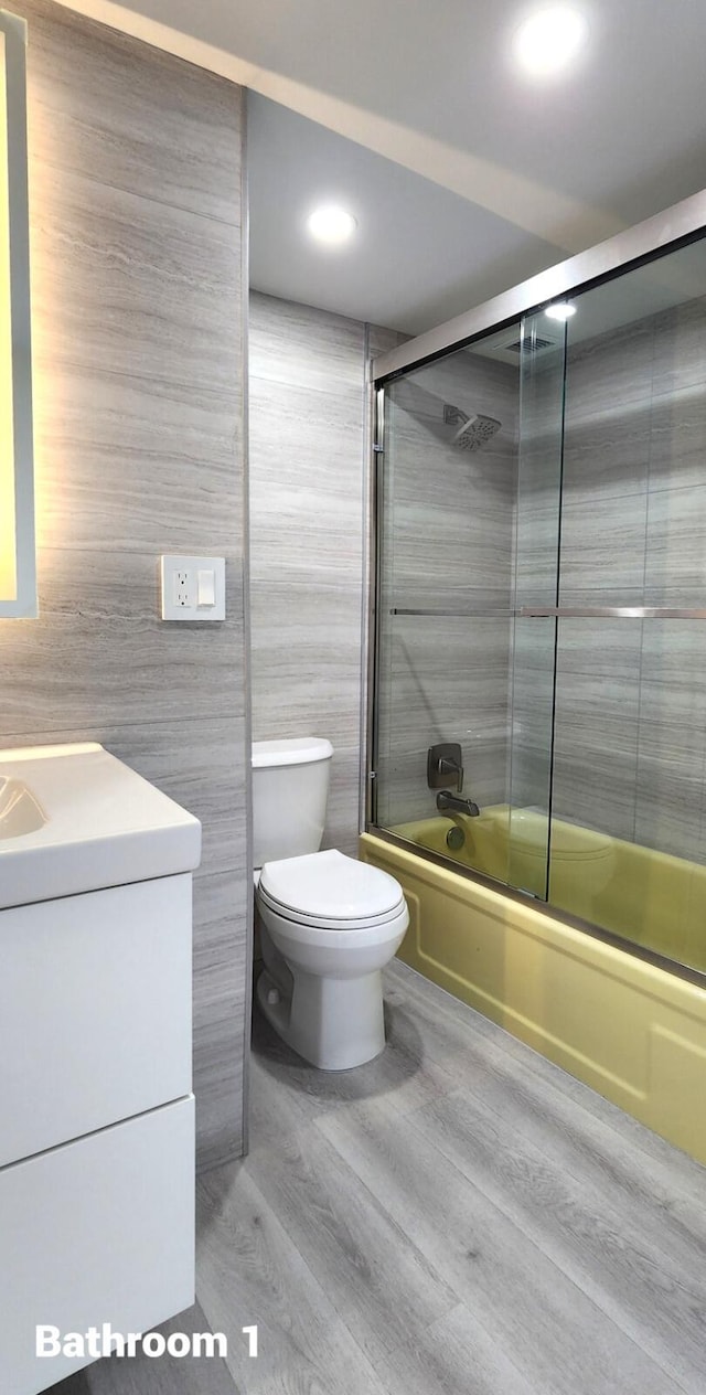 full bathroom featuring enclosed tub / shower combo, tile walls, vanity, wood-type flooring, and toilet