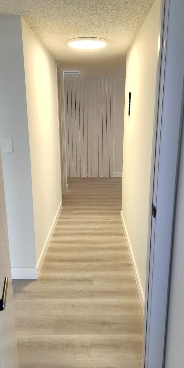 corridor with light hardwood / wood-style floors and a textured ceiling