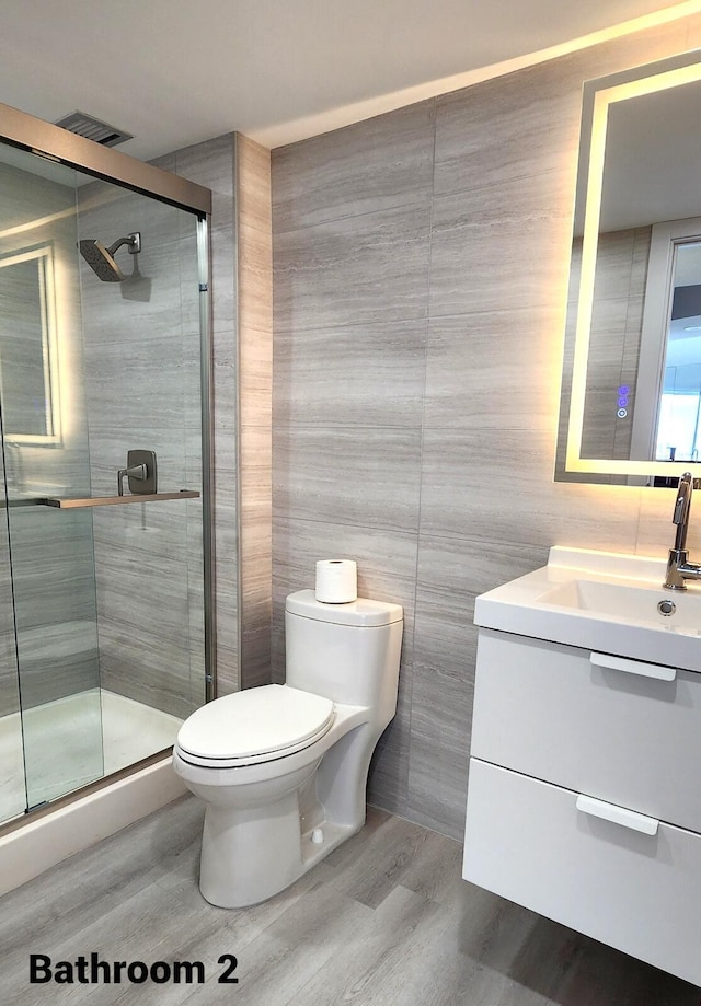 bathroom with toilet, a shower with shower door, wood-type flooring, tile walls, and vanity