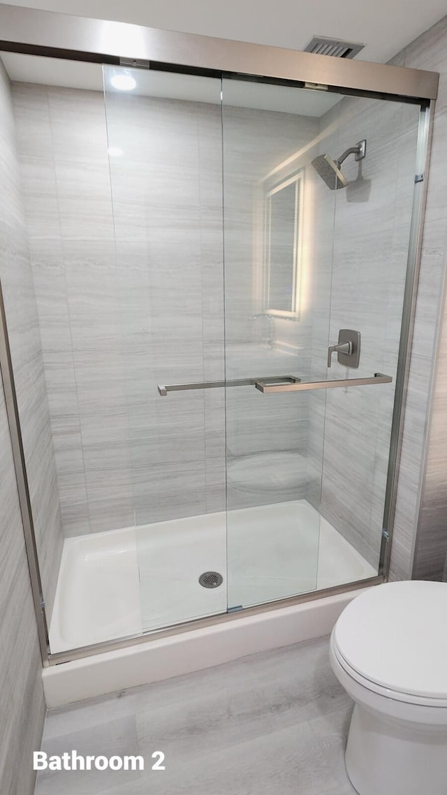 bathroom featuring toilet and a shower with shower door