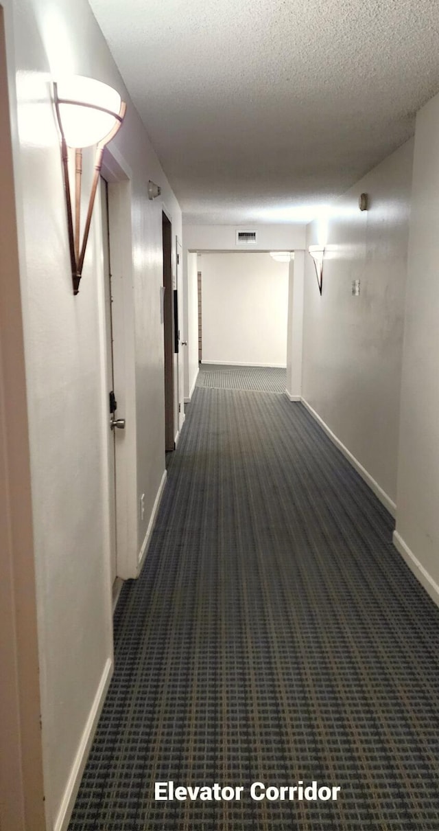 hallway featuring dark colored carpet and a textured ceiling