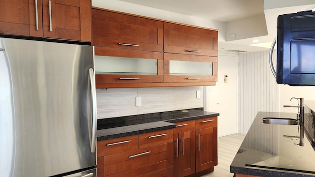 kitchen featuring sink, stainless steel refrigerator, dark stone countertops, and decorative backsplash