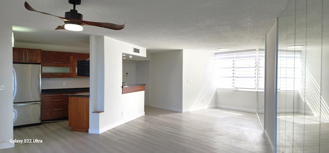 kitchen with dark countertops, light wood-type flooring, a textured ceiling, and freestanding refrigerator