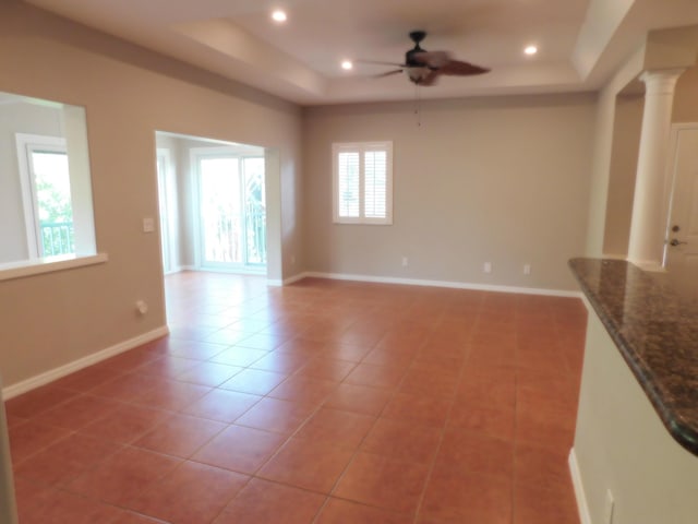 unfurnished living room featuring light tile patterned floors, ceiling fan, ornate columns, and a tray ceiling