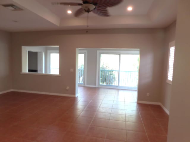 tiled empty room with ceiling fan, plenty of natural light, and a tray ceiling