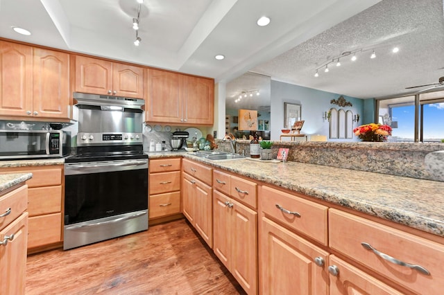 kitchen with stainless steel appliances, sink, a textured ceiling, light stone counters, and light hardwood / wood-style flooring