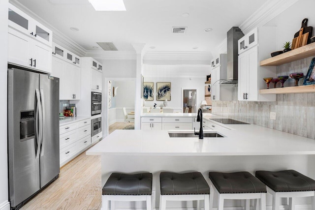 kitchen featuring stainless steel refrigerator with ice dispenser, wall chimney range hood, a kitchen bar, and kitchen peninsula