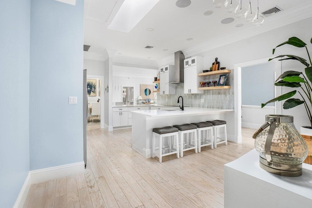 kitchen featuring a breakfast bar area, kitchen peninsula, wall chimney exhaust hood, and white cabinetry